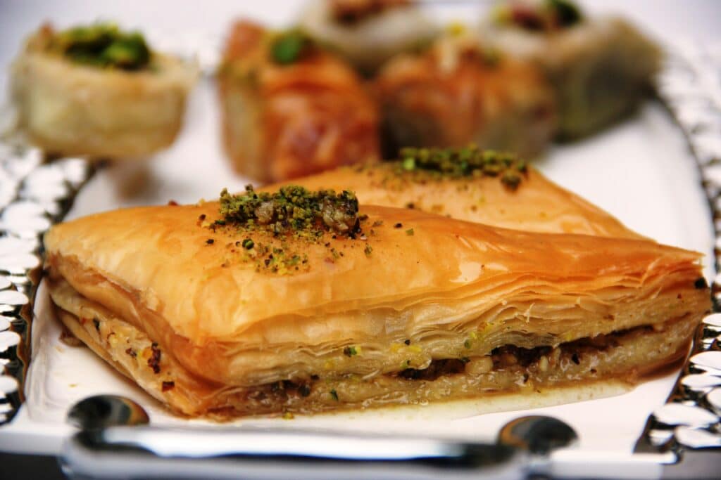 A vibrant still life depicting an array of traditional Greek sweets, captured in warm, natural lighting. In the foreground, a plate showcases a selection of delicate pastries, their intricate patterns and golden hues inviting the viewer to indulge. In the middle ground, a platter holds fragrant baklava, its layers of flaky phyllo and rich, nutty filling glistening. In the background, jars of honey and glass dishes filled with loukoumades, fluffy doughnuts drizzled with honey and cinnamon, create a cozy, homemade atmosphere. The composition evokes the comforting and indulgent essence of Greek dessert culture, with a focus on the artisanal craftsmanship and time-honored recipes that have been passed down through generations. Greek Cuisine Desserts