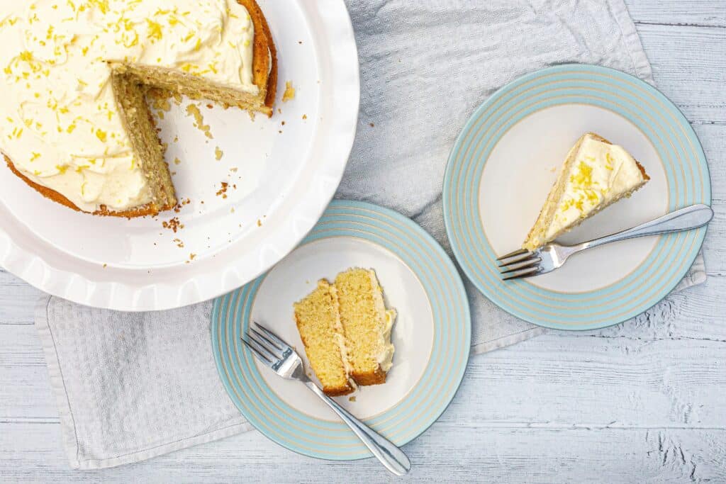 A deliciously moist and light lemon ricotta cake, with a golden brown top and a dusting of powdered sugar. The cake is positioned on a rustic wooden table, surrounded by fresh lemon slices and sprigs of thyme, creating a natural, earthy composition. Soft, diffused lighting from the side gently illuminates the cake's texture and highlights the fluffy, airy crumb. The scene evokes a sense of warmth, simplicity, and the refreshing essence of a lighter, brighter lemon dessert. A deliciously moist and light lemon ricotta cake