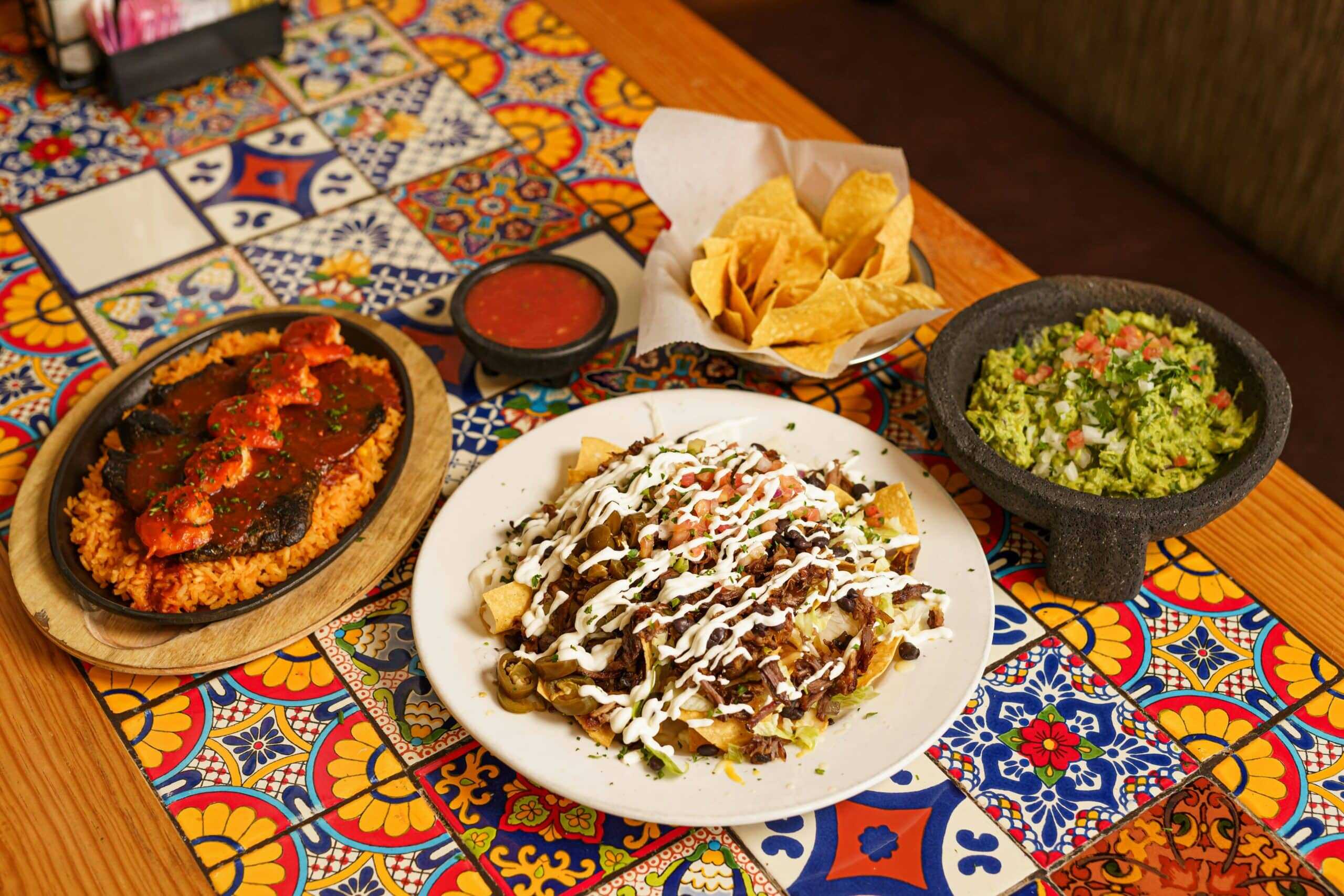 Colorful Mexican brunch spread with guacamole, nachos, rice with shrimp, and creamy beef nachos.