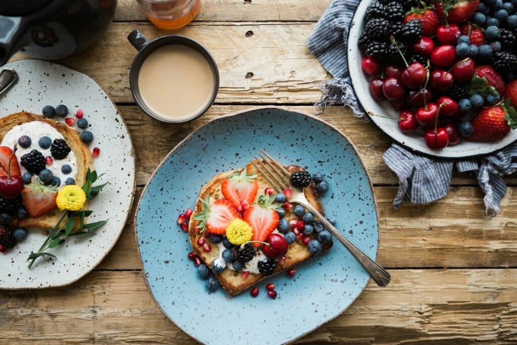 Vegetarian brunch menu inspiration featuring a rustic wooden table set with an assortment of fresh, colorful dishes. In the foreground, a platter of avocado toast garnished with microgreens and a drizzle of olive oil. In the middle ground, a bowl of creamy vegetarian quiche accompanied by a side salad of mixed greens and cherry tomatoes. In the background, a variety of baked goods such as flaky croissants and hearty whole grain muffins. Soft, diffused natural lighting filters through the window, creating a warm, inviting atmosphere. The scene captures the rise of a vibrant vegetarian brunch culture, showcasing innovative plant-based cuisine.