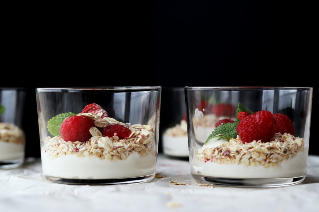 A vibrant and appetizing yogurt parfait, with layers of creamy Greek yogurt, fresh berries, and crunchy granola. The parfait is arranged in a tall glass, catching the warm morning light filtering through a nearby window. The berries, such as juicy raspberries and blueberries, are artfully scattered, creating a visually stunning contrast against the smooth, white yogurt. The granola sprinkled on top adds a lovely texture, with hints of toasted oats and caramelized nuts. The entire scene is captured with a soft, natural lighting, emphasizing the parfait's freshness and healthfulness. This image perfectly encapsulates the appeal of a delicious and nutritious yogurt parfait as the perfect breakfast. Yogurt Parfait Recipe