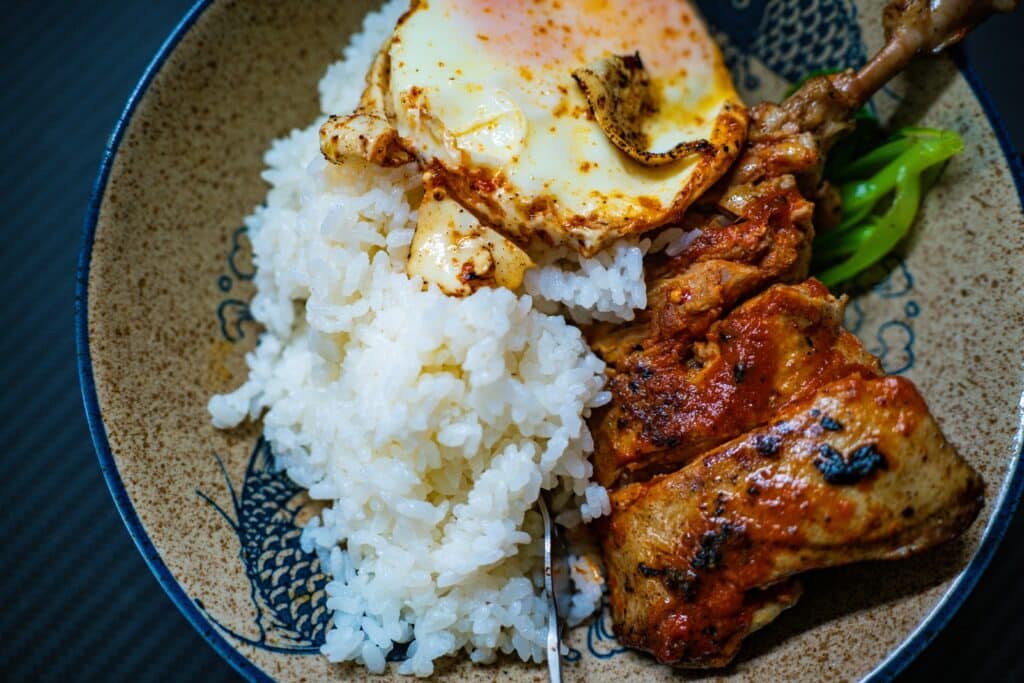 A delectable chicken and egg dish set against a cozy, rustic background. In the foreground, a perfectly cooked chicken breast rests atop a fluffy bed of scrambled eggs, with the yolks gently spilling out. The middle ground features a simple wooden table, adorned with a checkered cloth and a small vase of fresh herbs. Warm, soft lighting illuminates the scene, casting a comforting glow and highlighting the mouthwatering textures of the food. The background is a subtle, muted scene, hinting at a homely kitchen or dining area, allowing the dish to take center stage. The overall composition conveys a sense of harmony and simplicity, showcasing the timeless pairing of chicken and eggs as a delicious and satisfying comfort food. Chicken and Egg Recipe